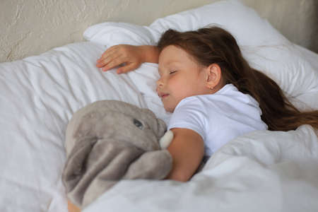 Cute child little girl sleeps in the bed with a toy elephant