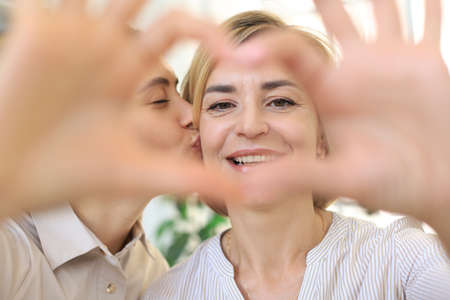 Happy beautiful adult woman and her daughter forming a heart with their hands while hugging, smiling. Mother's day. Concept of love, familyの写真素材