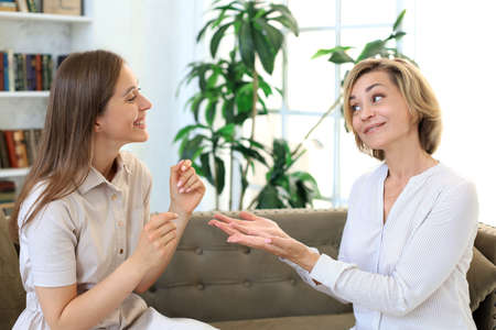 Happy middle aged mother and daughter talking on sofa in living room