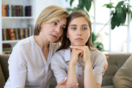 Concerned middle aged mother and adult daughter sit on couch having serious conversation, listen to...