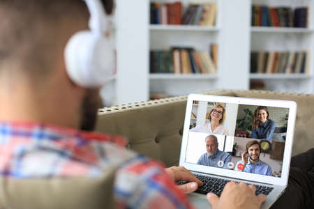 Businessman in headphones lying on sofa speak talk on video call with colleagues on online briefing...