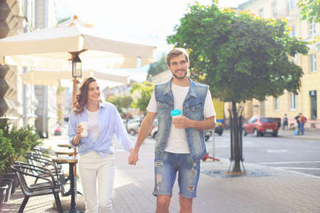Image of lovely happy couple in summer clothes smiling and holding hands together while walking...