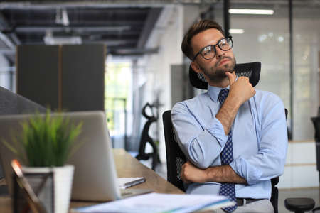 Focused businessman thinking at modern office into report file calculating stock market earnings,...