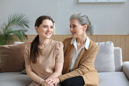 Beautiful mother and daughter. Cheerful young woman is embracing her middle aged mother in living...