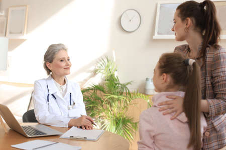 Mother and child in the doctor office meeting the pediatrician, they are sitting at desk in hospital