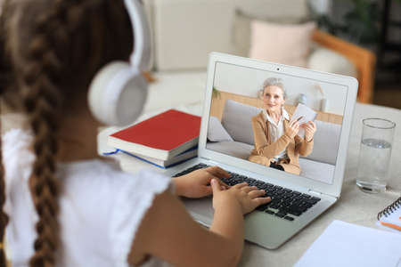 Distance learning. Cheerful little girl girl in headphones using laptop studying through online...
