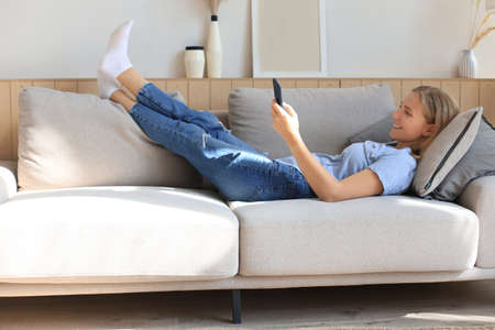 Pretty girl using her smartphone on couch at home in the living roomの写真素材