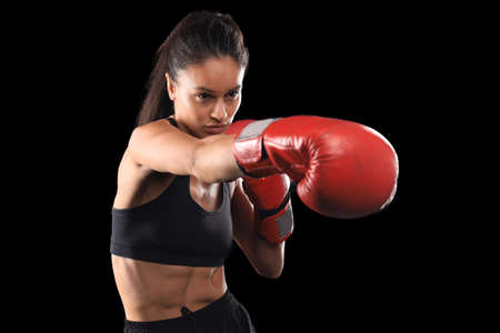 Kickboxing woman in activewear and red kickboxing gloves on black background performing a martial arts kick. Sport exercise, fitness workoutの写真素材