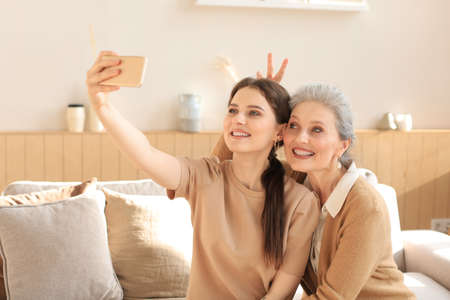 Happy middle aged mother and daughter taking selfie at home