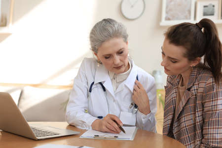 Middle aged female doctor therapist in consultation with patient in officeの写真素材