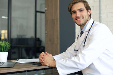 Handsome friendly young doctor on hospital corridor looking at camera, smiling