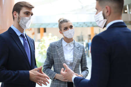 Three young businessmen wear preventive masks during epidemy, stand and discuss business at an office meeting.の写真素材