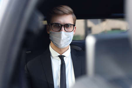 Thoughtful confident businessman in medical mask looking at camera while sitting in the carの写真素材