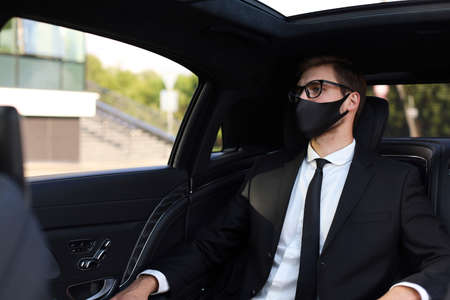 Thoughtful confident businessman in medical mask looking away while sitting in the carの写真素材