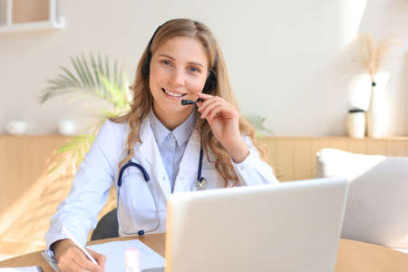 Friendly doctor working online with a laptop sitting in a desk in a consultation