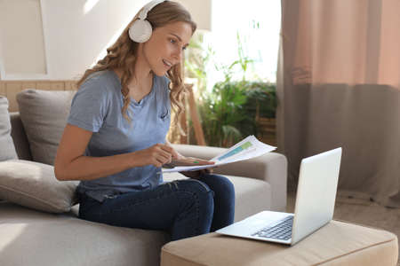 Smiling girl sit near couch watching webinar on laptop. Happy young woman study on online distant...