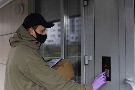 Courier in medicine mask and gloves with parcel calls the intercom to deliver the order to the...