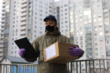 Courier in face mask with a parcel at the entrance of home verifies the information in the documentsの写真素材