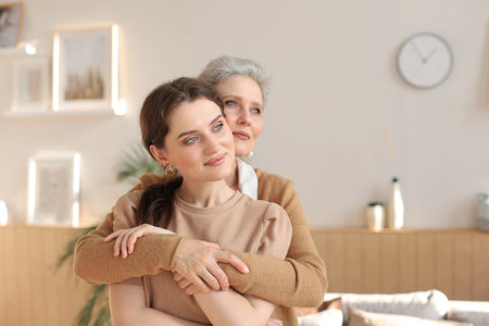 Portrait of old mother and mature daughter hugging at home. Happy senior mom and adult daughter embracing with love on sofaの写真素材