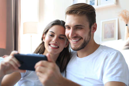 Happy couple enjoying media content in a smart phone sitting on a couch at home