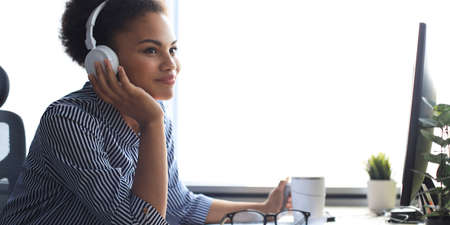 Young african american woman having a break and listening music in headphones sitting on working placeの写真素材