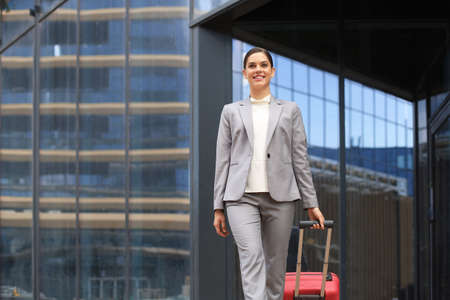 Portrait of successful business woman traveling with case at airport. Beautiful stylish female travel with luggageの写真素材