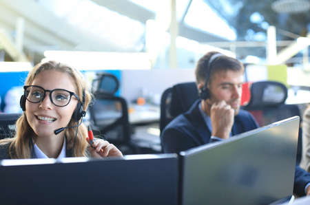 Female customer support operator with headset and smiling, with collegues at backgroundの写真素材