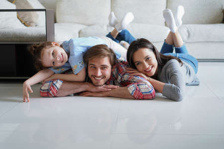 Young caucasian family with small daughter pose relax on floor in living room, smiling little girl kid hug embrace parents, show love and gratitude, rest at home togetherの写真素材
