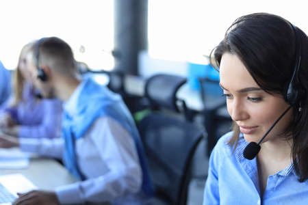 Female customer support operator with headset and smiling, with collegues at background