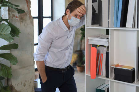 Sad worker in medical mask standing in officeの写真素材