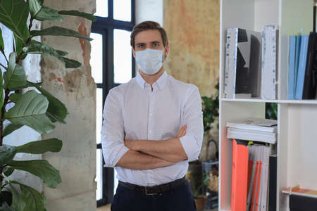 Young businessman in medical mask standing in modern officeの写真素材