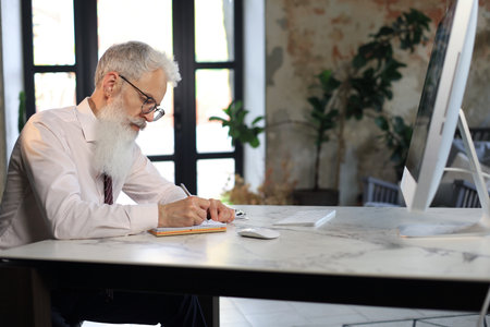 Focused mature businessman working and taking notes in his modern office