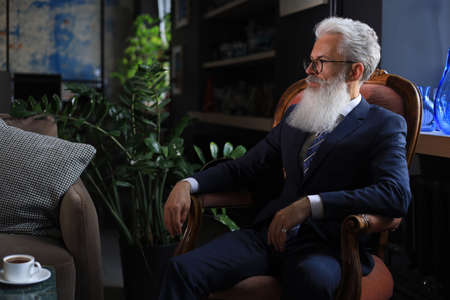 Thoughtful confident handsome businessman thinking while sitting on armchair in his modern office...