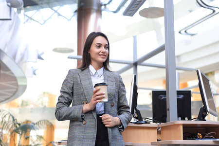 Attractive businesswoman standing with coffee near desk in the officeの写真素材
