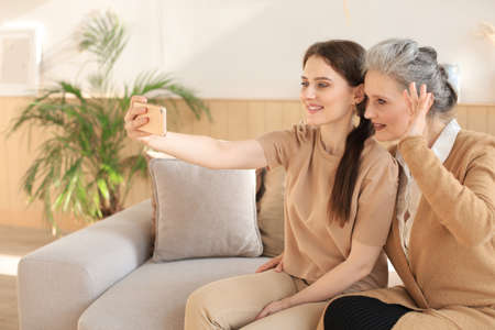 Happy middle aged mother and daughter taking selfie at homeの写真素材