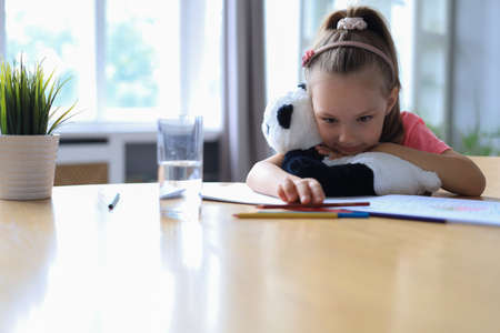Sad little girl sitting in the table with a toy panda bear while sitting in living room at homeの写真素材