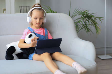 Distance learning. Cheerful little girl using laptop computer studying through online e-learning...