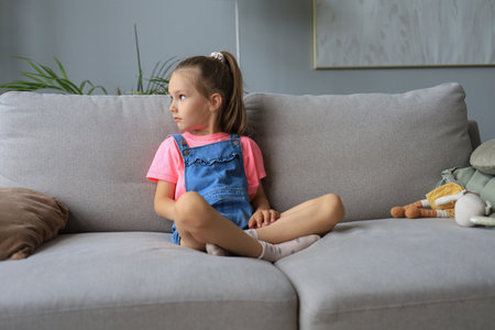 Sad little girl sitting on sofa alone at homeの写真素材