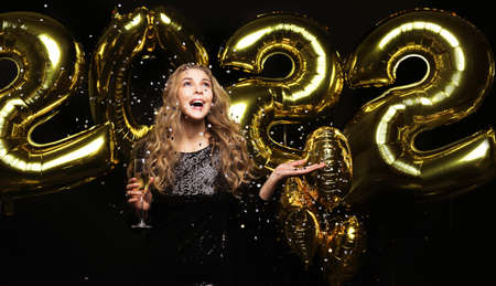 Happy gorgeous girl in stylish sexy party dress holding gold 2022 balloons, having fun at Christmas...