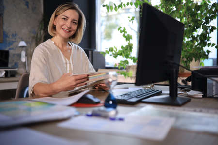 Attractive middle aged woman working at office, using contemporary desktop computerの写真素材