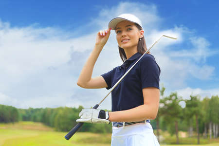 Professional female golfer holding golf club on field and looking away. Young woman standing on golf course on a sunny day.の写真素材