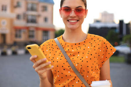 Portrait fashion woman in yellow dress walking on street and holding smartphone in her hand.