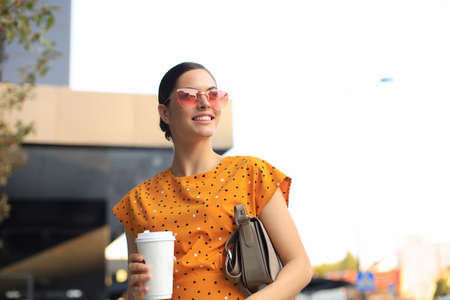 Portrait fashion woman in yellow dress holding coffee cup walking on street of the city, smiling to...