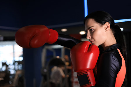 Female in red boxing gloves and sportive wear stands in a rack in the boxing hallの写真素材