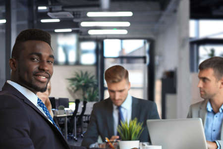 Smiling confident African businessman in a meeting with a colleagues seated at a conference table in the office.の写真素材
