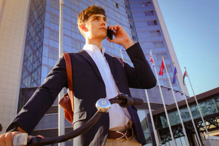 Young businessman with bicycle and smartphone on city street.の写真素材