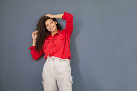 Young woman in red shirt standing against gray wall.の写真素材