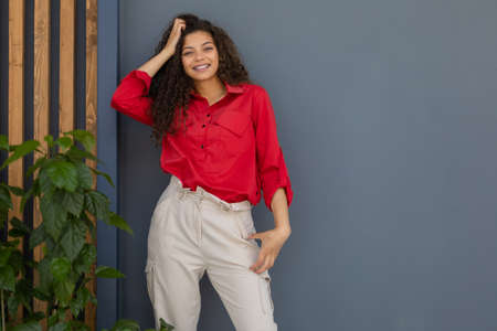 Young woman in red shirt standing against gray and wooden wall.