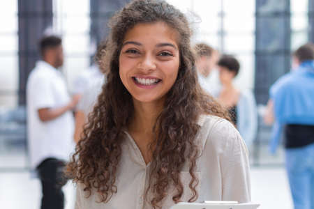 Smiling young woman standing with documents in the office with collegues on the background