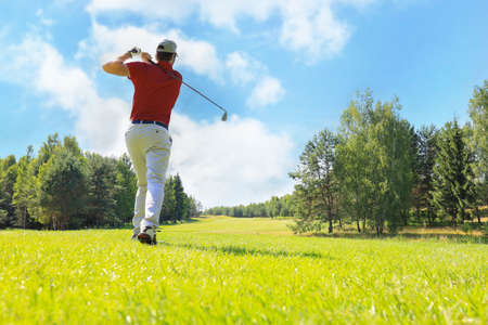 Full length of golf player playing golf on sunny day. Professional male golfer taking shot on golf courseの写真素材